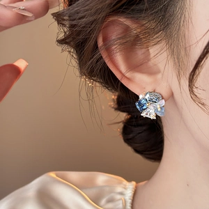 Detailed close-up of crystal flower cluster earring with blue gems and pearl on model