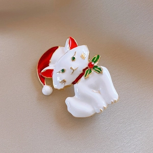 Close-up of a Christmas cat brooch with white enamel, red hat and green holly on beige fabric
