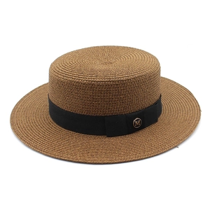 Détail du chapeau canotier à bord plat avec ruban noir et boucle métallique dorée 'M'