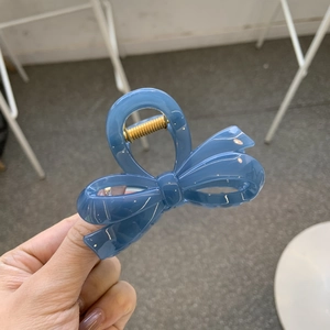 Detail of blue bow hair claw clip showing a glossy finish and a sturdy golden metal spring
