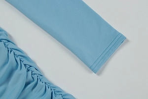 Detail of light blue dress showing ruched fabric texture and fine stitching on the sleeve