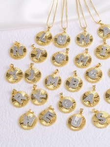 Close-up of gold disc pendants with zircon-encrusted silver letters and sunray textures