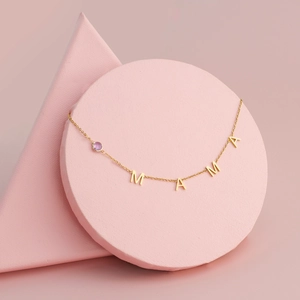 Detailed macro shot of a gold MAMA pendant necklace with a purple gem on pink geometric stands