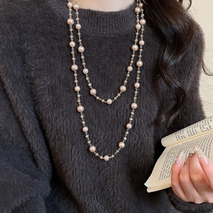 Detail of layered double-strand long pearl necklace with glass beads on grey sweater