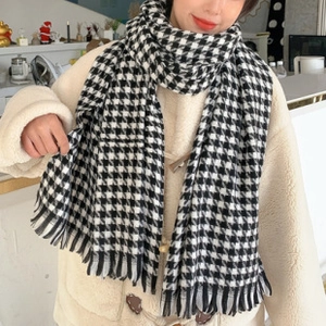 Detail of soft black and white houndstooth scarf with tassels on female model in a cafe