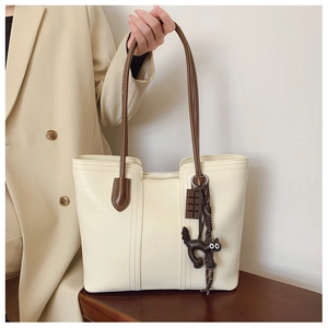 Detail of creamy white tote bag featuring brown straps and cute cat charms for daily use