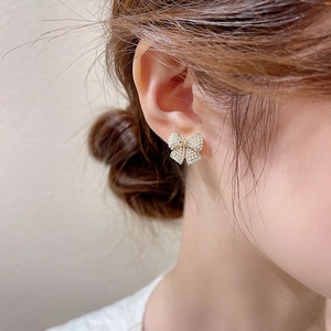 Macro shot of gold bow earrings featuring micro pearls and cubic zirconia on a model