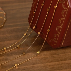 Double-layered gold titanium necklace with cube beads draped over a red jewelry box