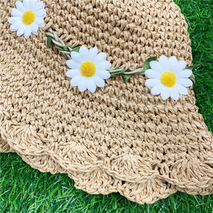 Detailed texture of hand-woven straw hat featuring floral daisy and green leaf trim