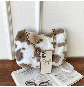 Close-up of faux fur tote bag with cow print pattern and golden chain strap detail