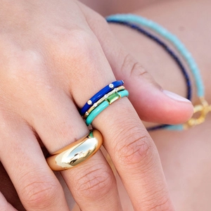 Detail of layered gold rings with colorful enamel and rectangular green gemstone on model