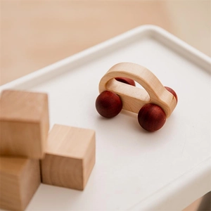 Close-up of a natural walnut wood toy car with dark red spherical wheels and soft focus