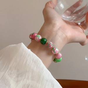 Detail shot of a gold-plated bracelet with pink floral and green glass beads on a model