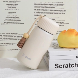 Mini cream insulated water bottle with decorative tassel tassel on white book