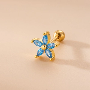 Gold flower stud earrings with blue zircon stones and screw back closure on beige background