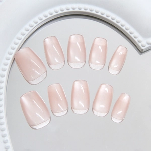 Press-on nails in nude pink cat-eye design with classic white French tips on vintage tray
