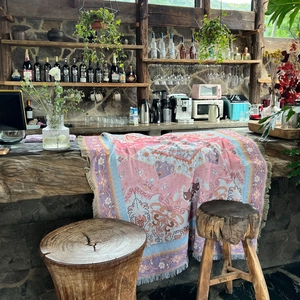 Pink bohemian woven blanket with geometric patterns and fringe on a wooden counter