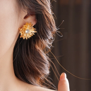 Detail of golden flower earring with crystal center worn by model in warm lighting
