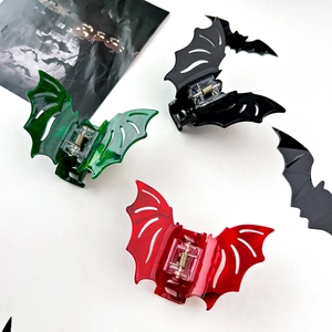 Detailed view of four bat-shaped acrylic hair claws in glitter green, marble red, and black