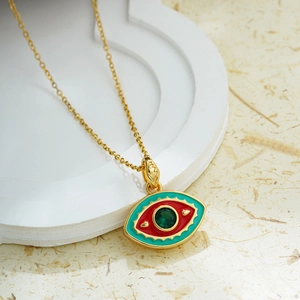 Macro detail of 18K gold evil eye pendant with red and teal enamel and green crystal