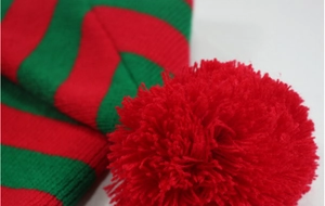 Close-up of festive red plush pom-pom and green striped knitted wool texture