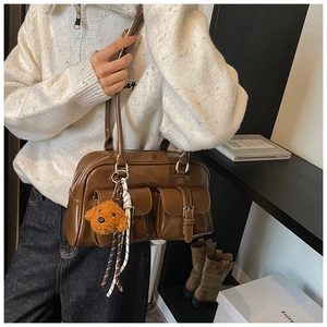 Detail of a brown glossy Boston bag with front pockets and a cute teddy dog plush pendant