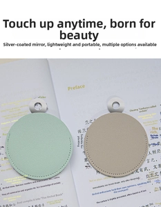 Close-up of portable leather makeup mirrors in mint green and beige on a book