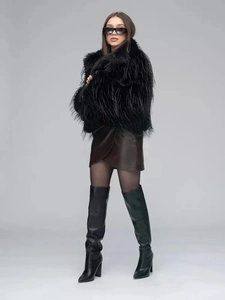 Detailed view of women's thick black faux fur coat styled with leather skirt and boots