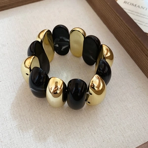 Macro detail of elastic bracelet showing glossy black resin and gold oval beads