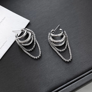Detail view of silver layered hoop earrings with zircon fringe chains on black textured base