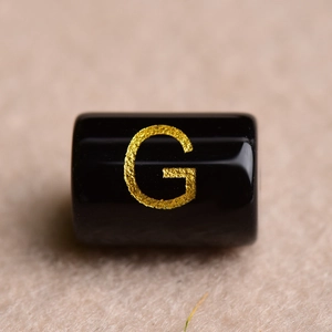 Macro shot of a black cylindrical bead featuring a gold-engraved letter G for DIY jewelry