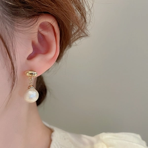 Detail showing elegant gold oval stud earring with white pearl pendant on model ear