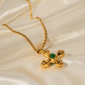 Macro view of 18k gold cross pendant featuring a green stone inlay on white silk fabric