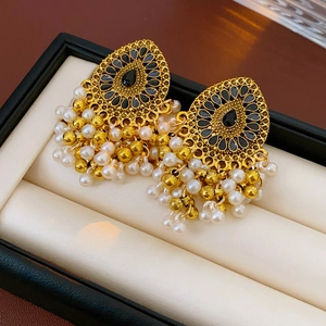 Détail de boucles d'oreilles vintage dorées avec incrustation noire et pompons en perles