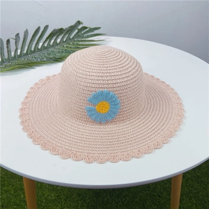 Vue détaillée d'un chapeau de paille rose orné d'une marguerite bleue au crochet.