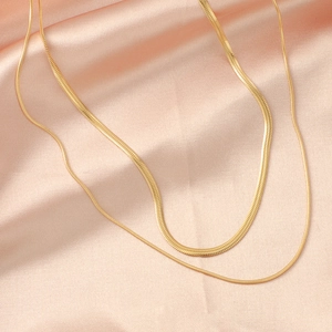 Double layered gold snake and flat blade chain necklace on pink silk fabric background