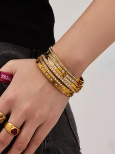 Dettaglio di più bracciali in acciaio inossidabile placcati oro 18k con zirconi sul polso