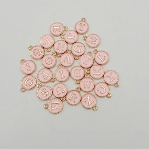 Flat lay of pink enamel round alphabet charms with gold metal frame for DIY jewelry