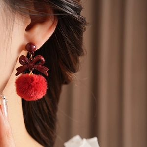 Close-up of red plush ball bow earrings worn by a model in a stylish profile view