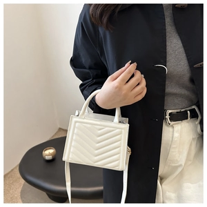 Detail of white cross-body lady bag featuring stylish V-quilted texture and gold hardware