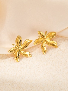 Macro detail of gold flower earrings featuring irregular lava texture on satin background