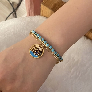 Double-layered gold chain bracelet with turquoise beads and palm tree pendant on wrist