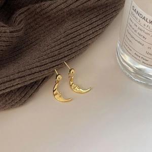 Detailed view of gold crescent moon stud earrings with face relief in a lifestyle setting