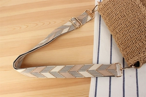 Detailed macro of a woven crossbody bag strap with chevron pattern and gold metal hardware