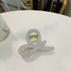 Detail of a creamy white glossy hair claw clip featuring a golden metal spring mechanism
