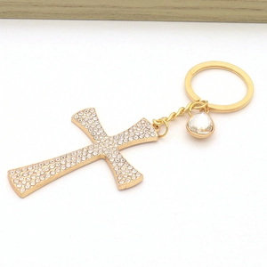 Detail of a golden cross keychain with shimmering rhinestones and a water drop crystal pendant