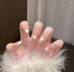 Détail d'ongles dégradés nude avec pointes French et petit ours blanc décoratif