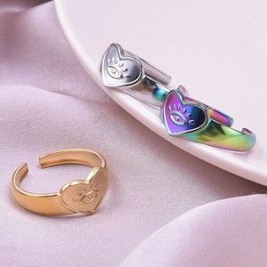 Dettaglio di anelli a cuore oro, argento e arcobaleno con incisione occhio su seta rosa