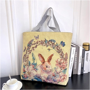 Detailed close-up of rabbit and floral embroidery on beige canvas tote bag with striped strap