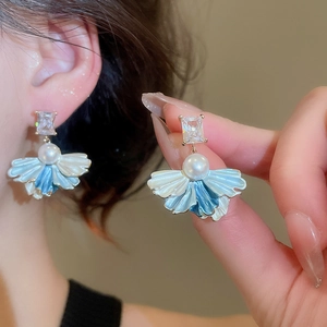 Close-up of fan-shaped pearl drop earrings with zircon studs being held on ear